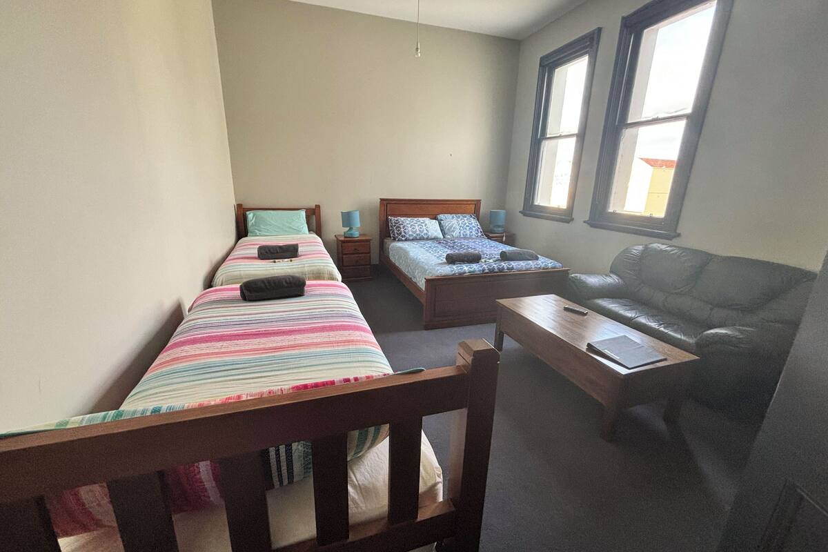 Une chambre avec deux lits simples, un banc en bois, un canapé en cuir et une petite table.