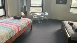 A small, well-lit room with a bed, a desk, and a chair. There is a window providing a view of the outside. - Australia Hotel Fremantle (Fremantle)