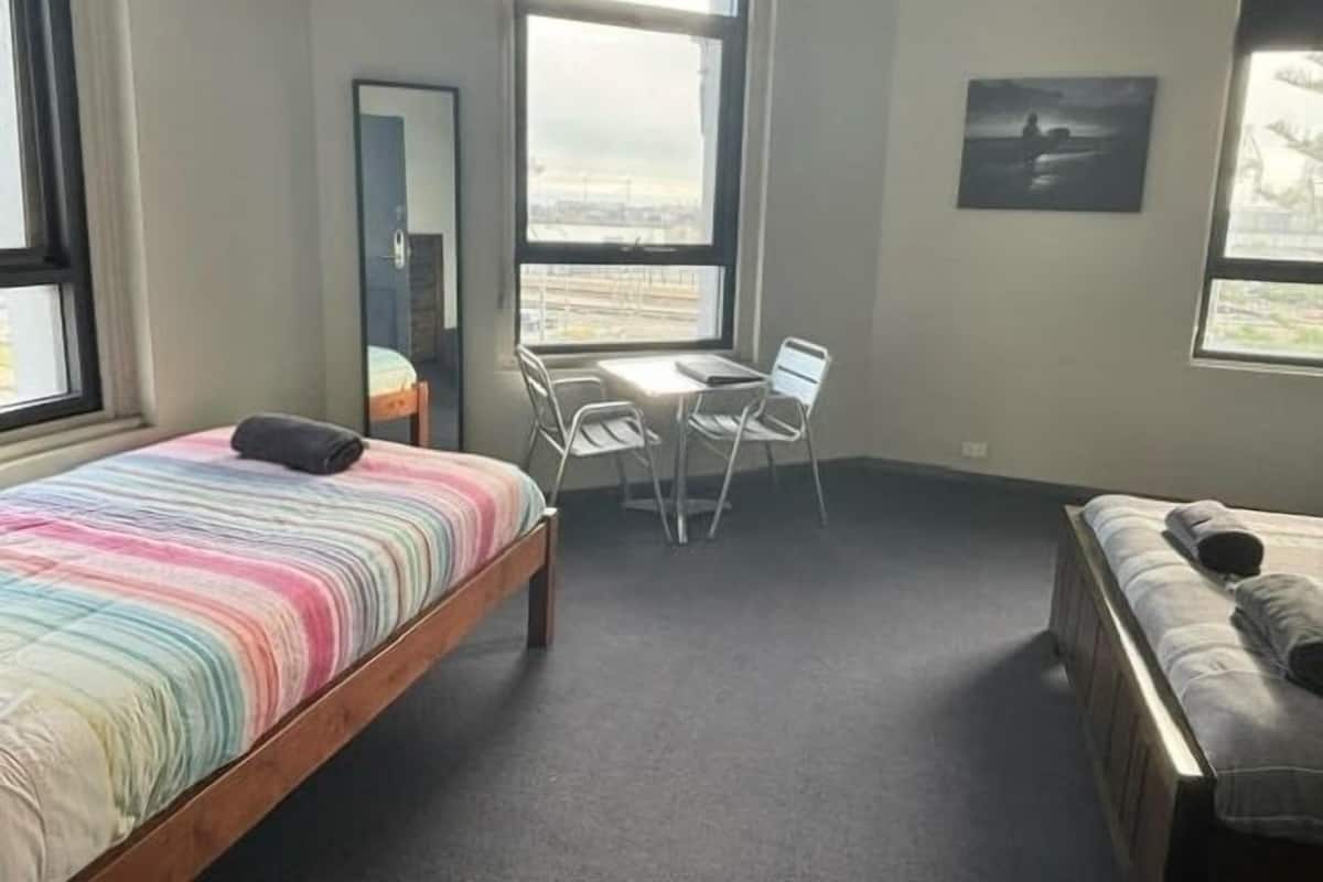 Une petite pièce bien éclairée, avec un lit, un bureau et une chaise. Une fenêtre offre une vue sur l’extérieur.