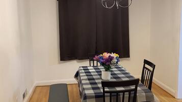 A dining area with a checkered tablecloth, black chairs, a bench, a chandelier, and a window with curtains.