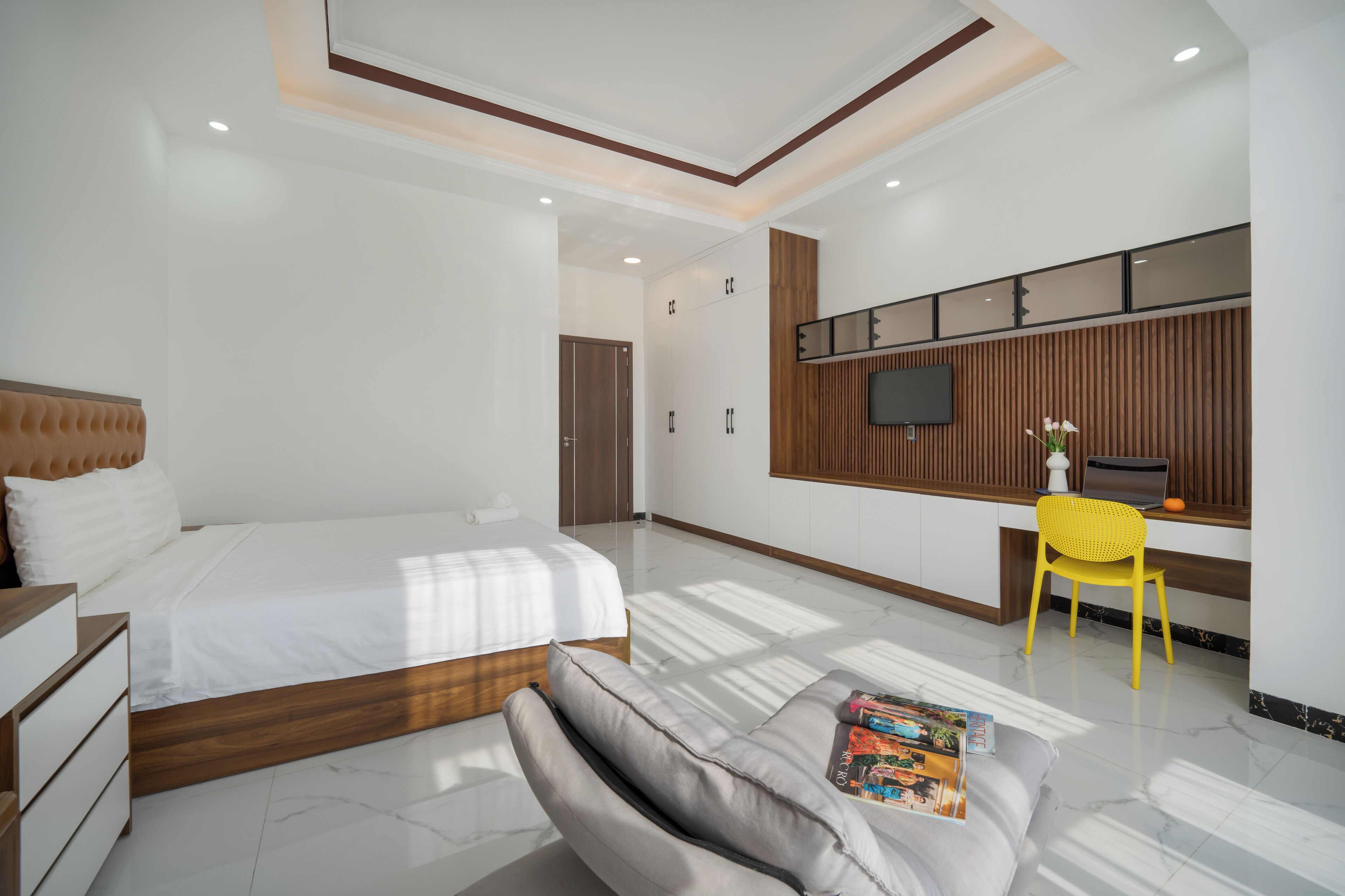 Quarto moderno com uma cama grande, uma escrivaninha com cadeira, televisão de tela plana e um pequeno vaso de planta.
