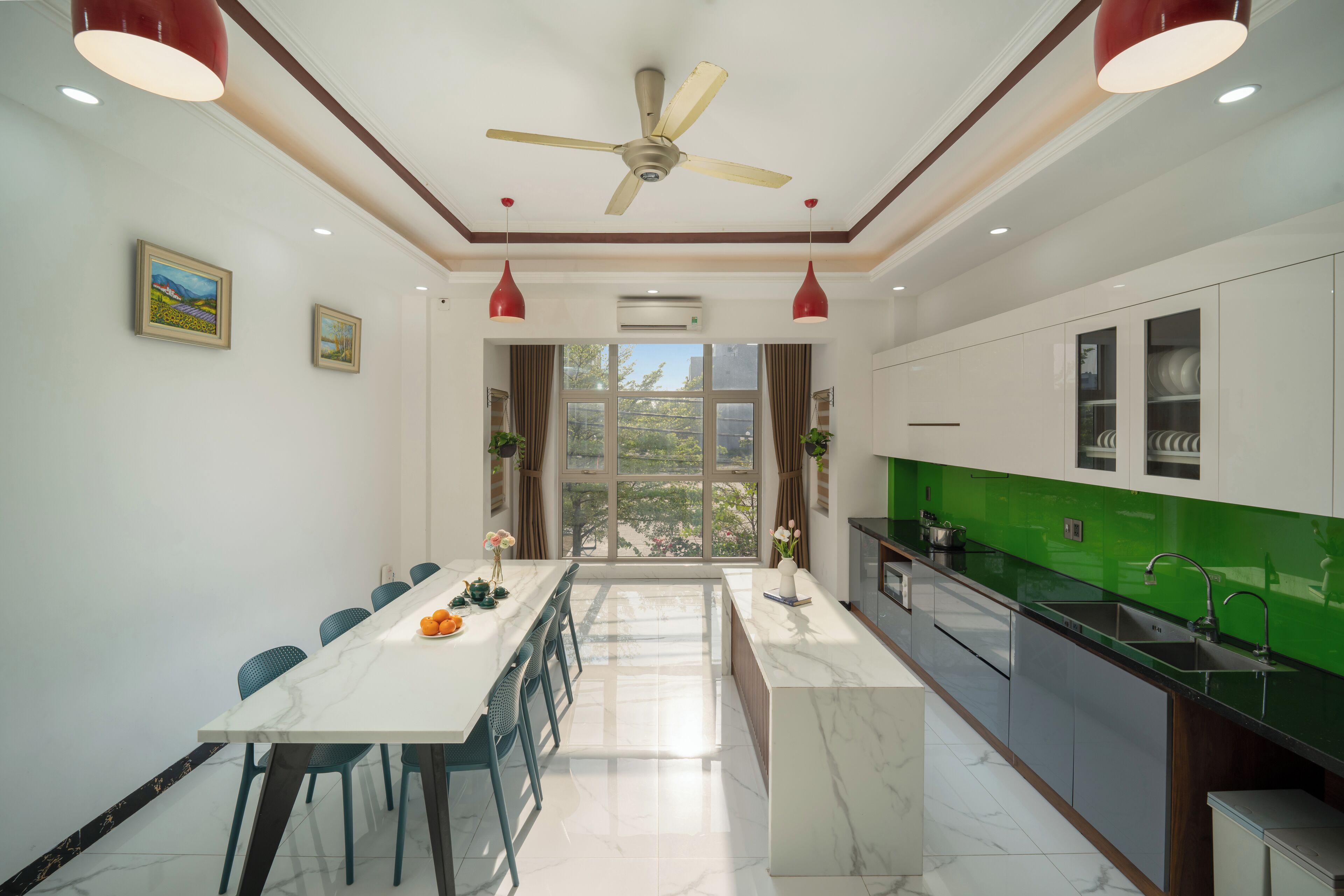 A modern kitchen with a marble countertop, a dining area with a white table and chairs, and a view through large windows.