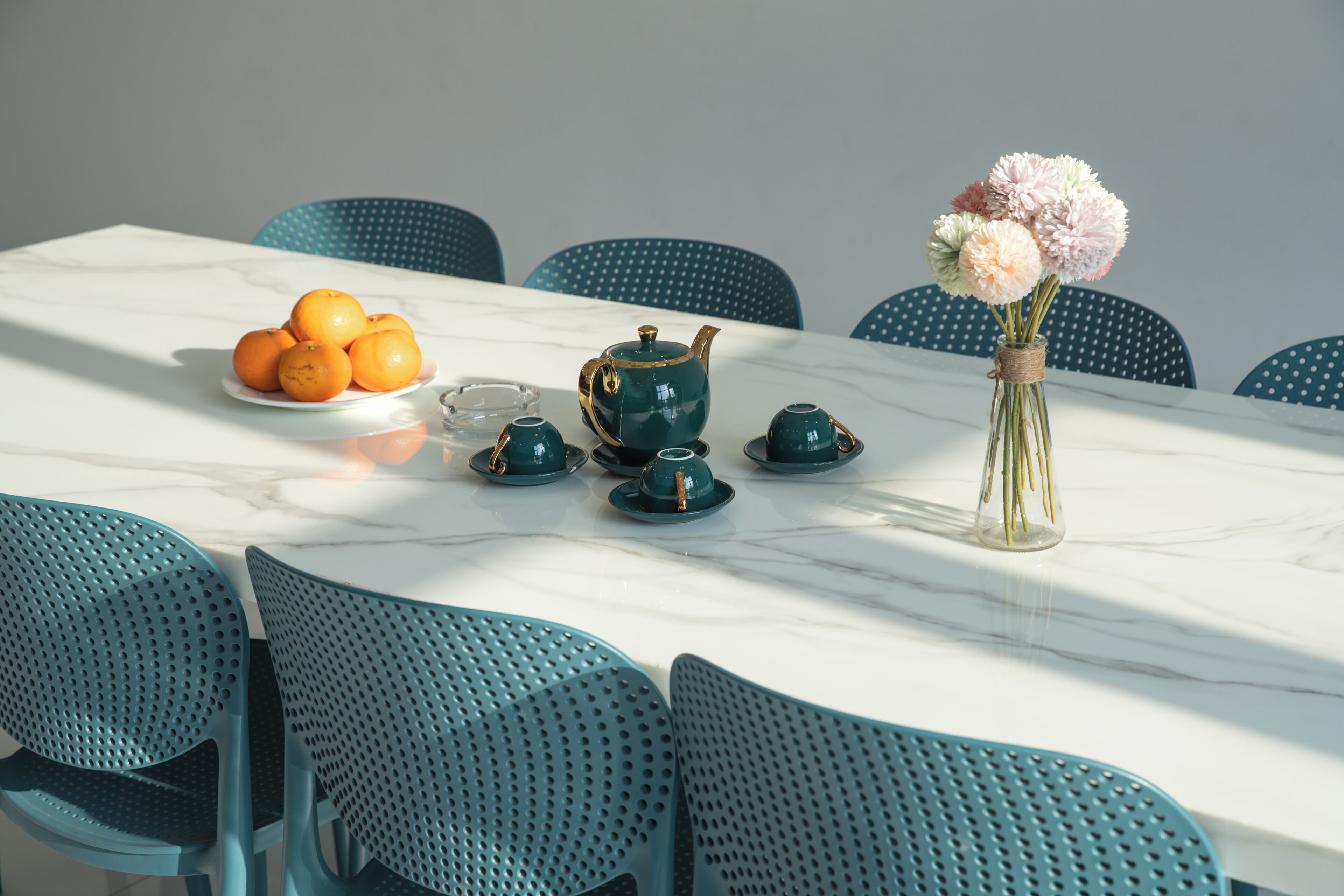 A table set with a green teapot, cups, and a vase of flowers.