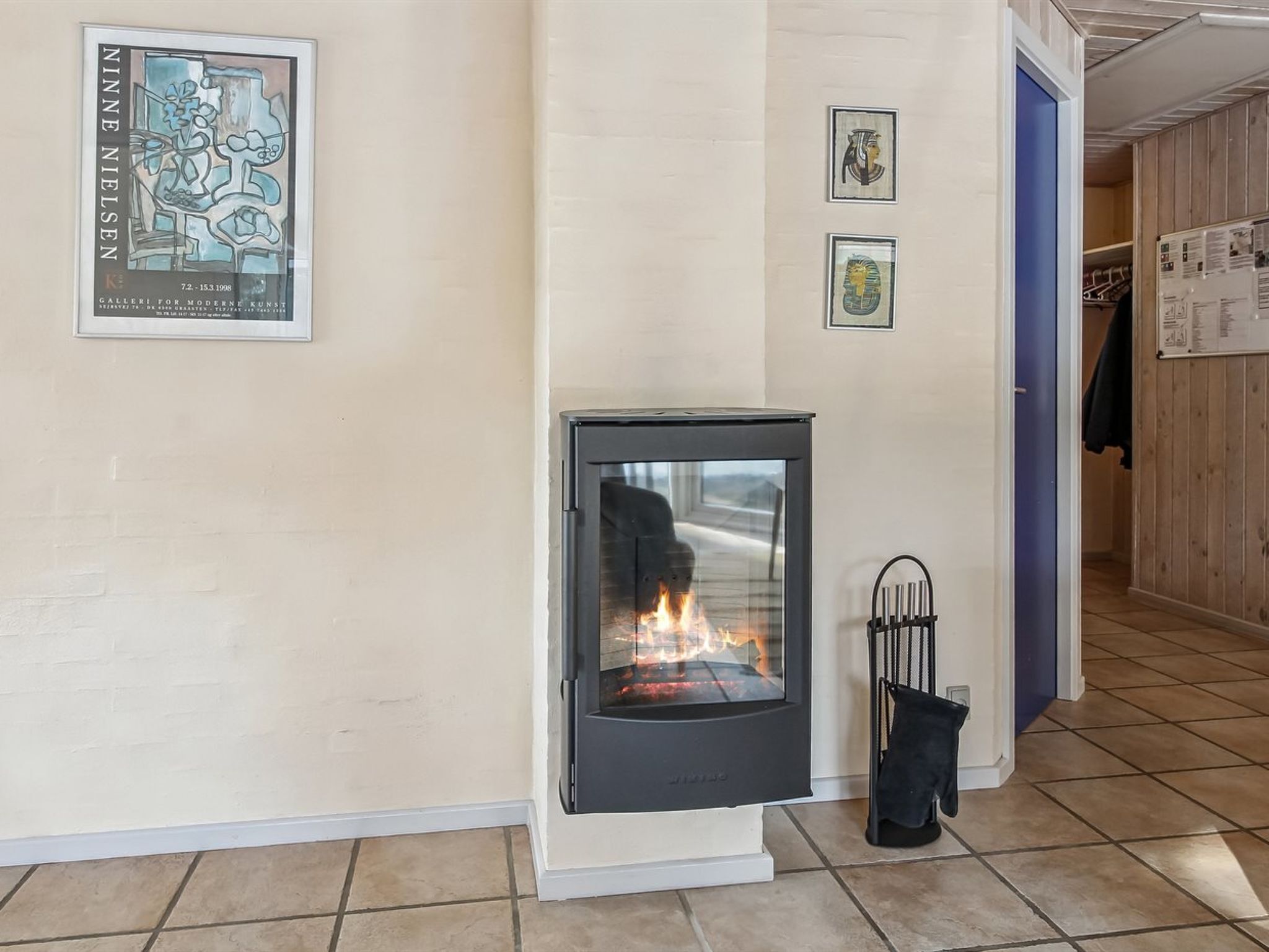 A room with a wood-burning stove, a poster on the wall, and a door leading to another room.