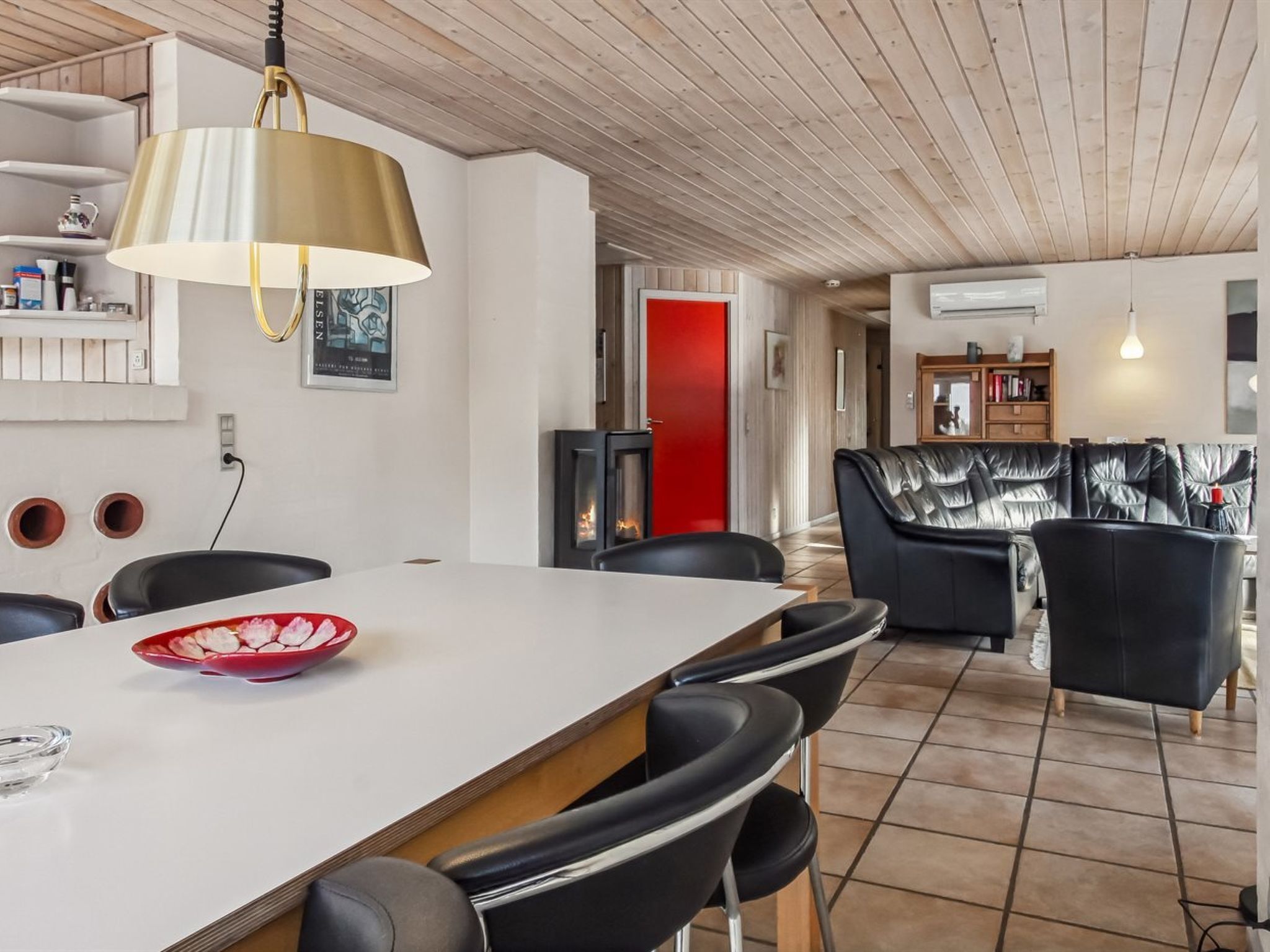 Une cuisine moderne avec un îlot central, des chaises noires, un saladier rouge et un luminaire suspendu.