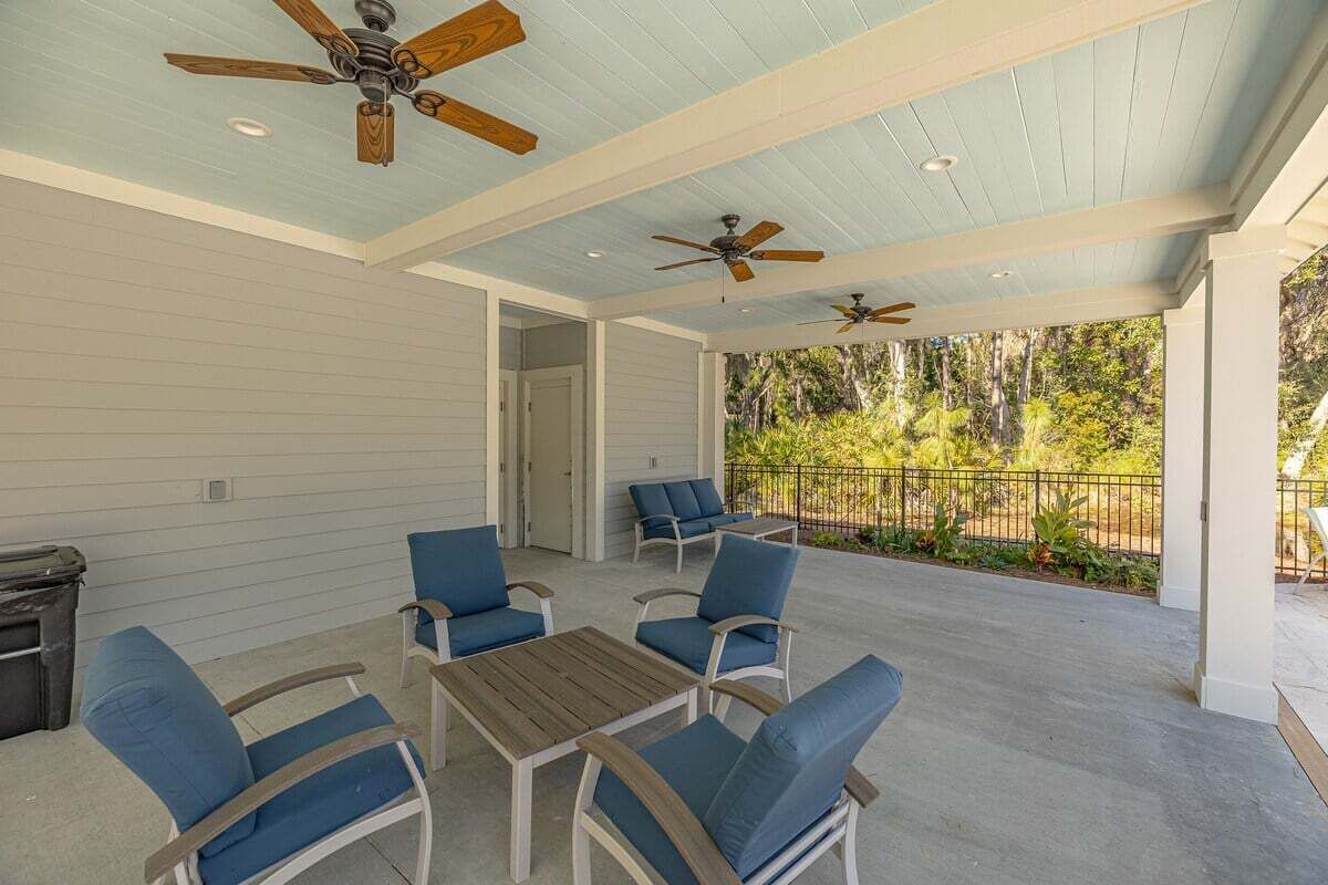 An outdoor covered patio with ceiling fans, blue cushioned chairs, and a wooden table.