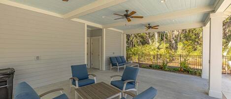 An outdoor covered patio with ceiling fans, blue cushioned chairs, and a wooden table.