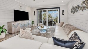 Una sala de estar moderna con un televisor de pantalla plana grande, un sofá, una mesa de centro y un balcón con mobiliario exterior.