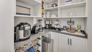 Una cocina con armarios blancos, cafetera, licuadora y despensa.