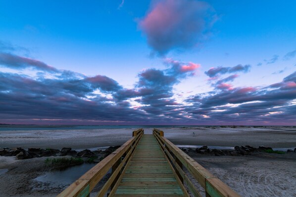 A wooden pier leading to a beach with a clear sky and clouds.