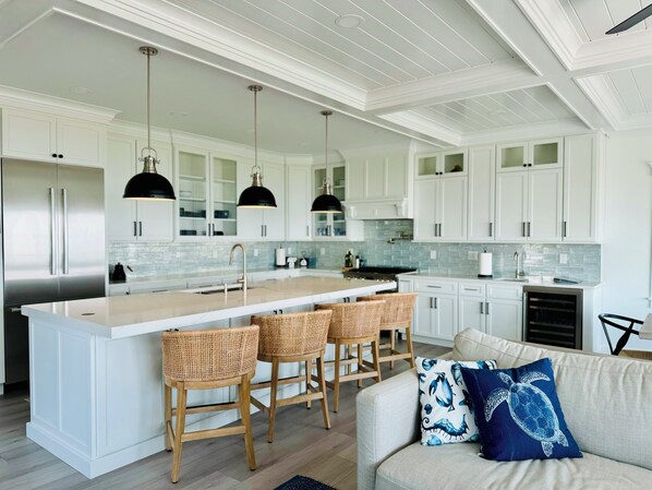Una cocina moderna con armarios blancos, una isla central con taburetes y luces colgantes, además de un horno empotrado.
