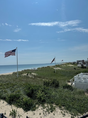Vista de una playa con banderas estadounidenses, una zona arenosa con vegetación y un edificio con terraza.