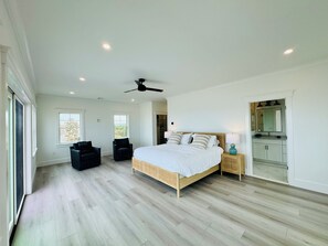 Un dormitorio amplio con una cama grande, un ventilador de techo y vistas al exterior a través de una ventana.