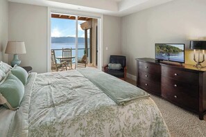 Quarto com cama, penteadeira, televisão, cadeira e vista para um lago através de uma porta de correr.