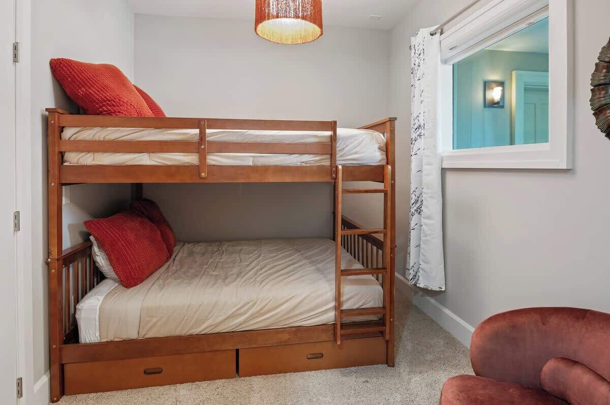 A bunk bed with storage drawers, a red pillow, and a hanging light fixture in a room with a window and a chair.