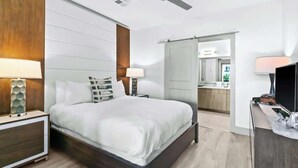 Ett modernt hotellrum med en stor säng, sängbord, en tv och ett badrum som syns genom en öppen dörr.