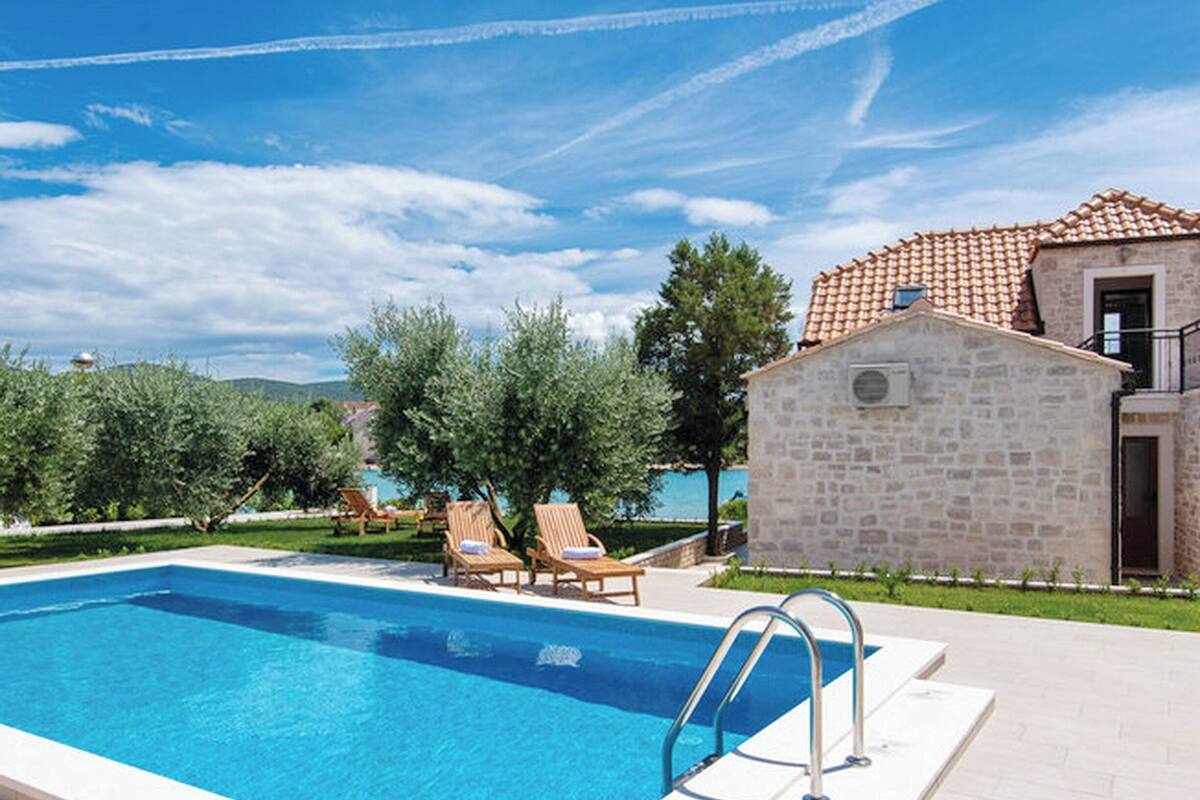 Une piscine avec des chaises longues, un bâtiment en pierre et un ciel dégagé.