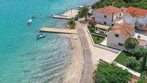 A coastal area with boats docked at a pier, a sandy beach, and residential buildings with red-tiled roofs. - Holiday Home Lovište (Orebic)