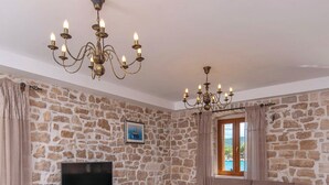 A living room with a stone wall, a large sofa, a wooden coffee table, a TV, and a chandelier. - Holiday Home Lovište (Orebic)