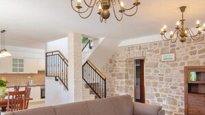 A spacious living room with a large beige sectional sofa, a wooden coffee table, and a stone wall. A staircase with a black railing leads to an upper level. - Holiday Home Lovište (Orebic)