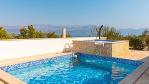 A rooftop swimming pool with a stone wall and a view of distant mountains. - Villa Anabella (Supetar)