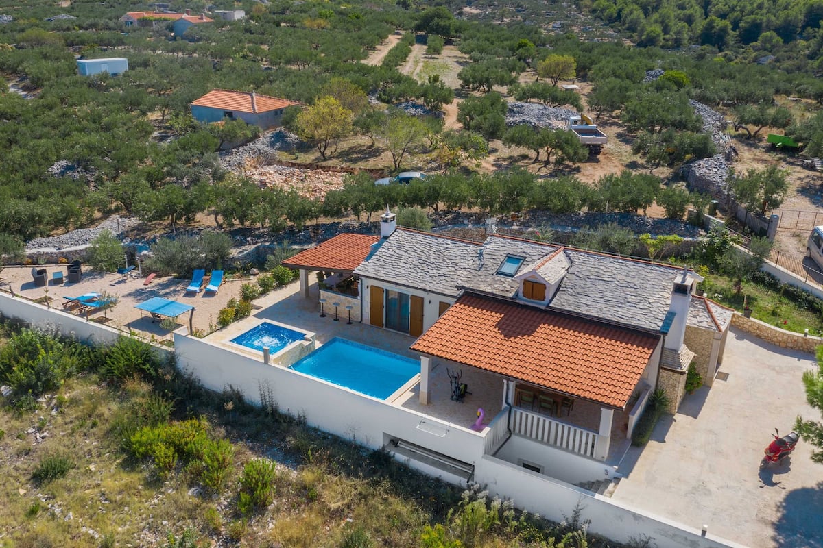 A two-story house with a swimming pool, a patio with outdoor furniture, and a stone roof.