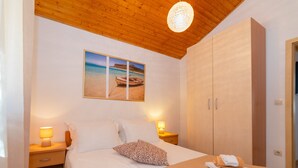 A bedroom with a bed, two bedside tables with lamps, a wardrobe, and a beach scene painting on the wall. - Villa Anabella (Supetar)