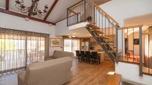A spacious living area with a high ceiling, a staircase to an upper level, a dining area with chairs, and a sofa. - Villa Anabella (Supetar)