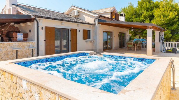 A swimming pool with a stone wall and a wooden deck. - Villa Anabella (Supetar)