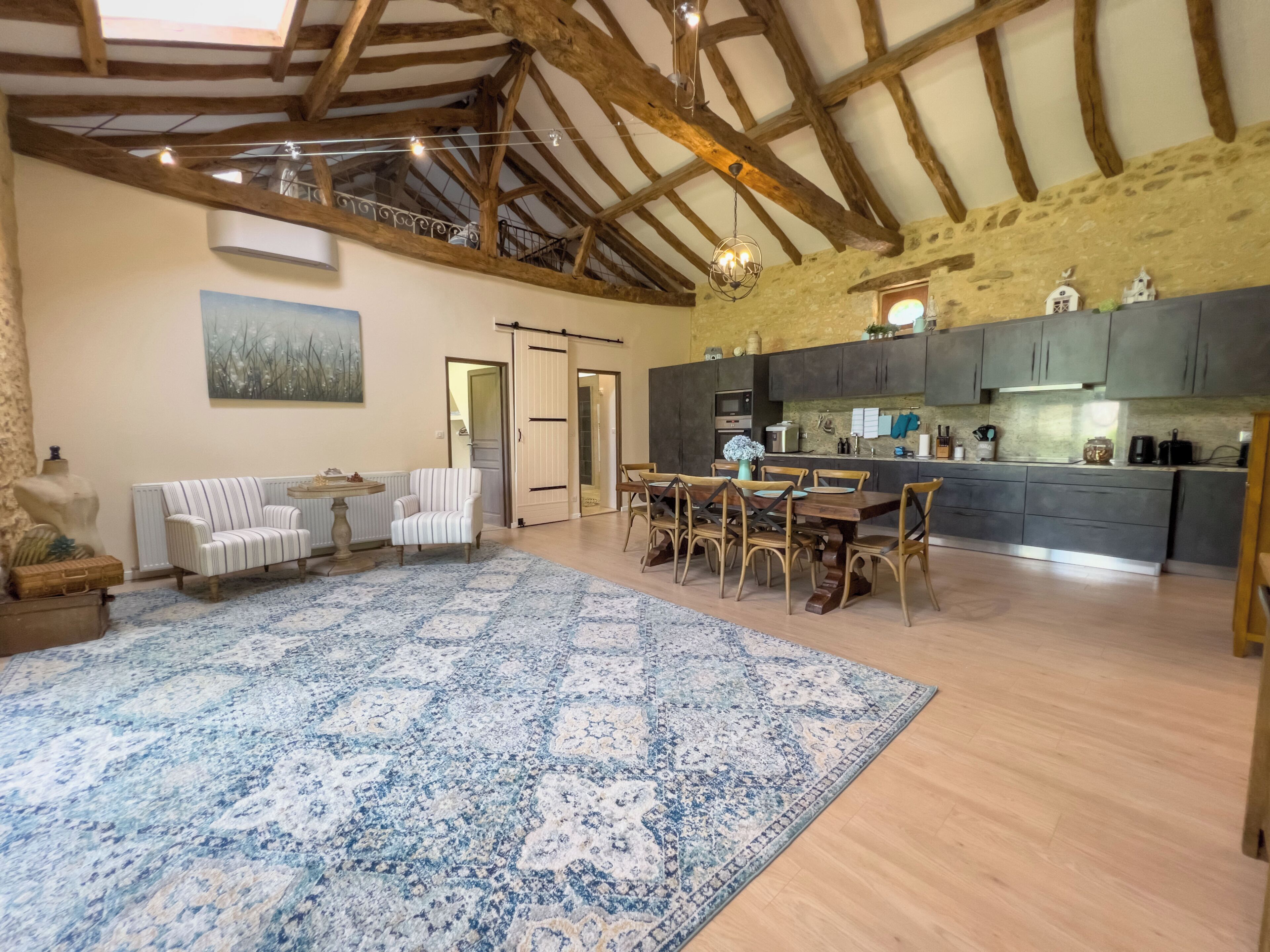 A spacious living area with a dining set, a large rug, and a kitchen with modern appliances.