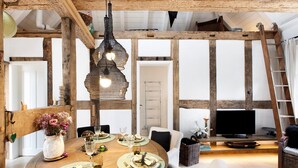 Een eethoek met een ronde tafel voor vier personen, een televisie op de achtergrond en een houten plafondconstructie.