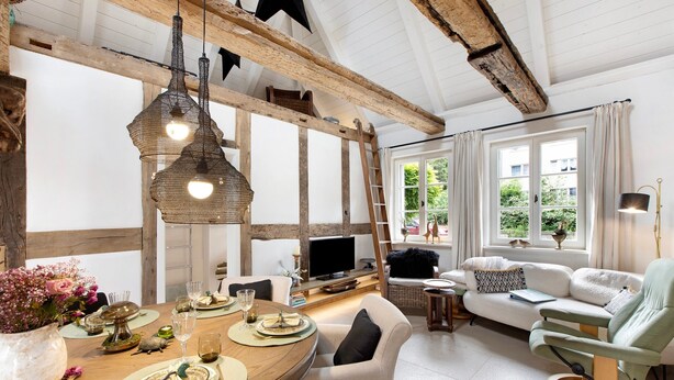 Een eetgedeelte met een houten tafel gedekt voor vier personen, een televisie en een bank met uitzicht op een raam.