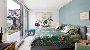 Een slaapkamer met een groot bed, uitzicht door een schuifdeur en een kunstwerk aan de muur.