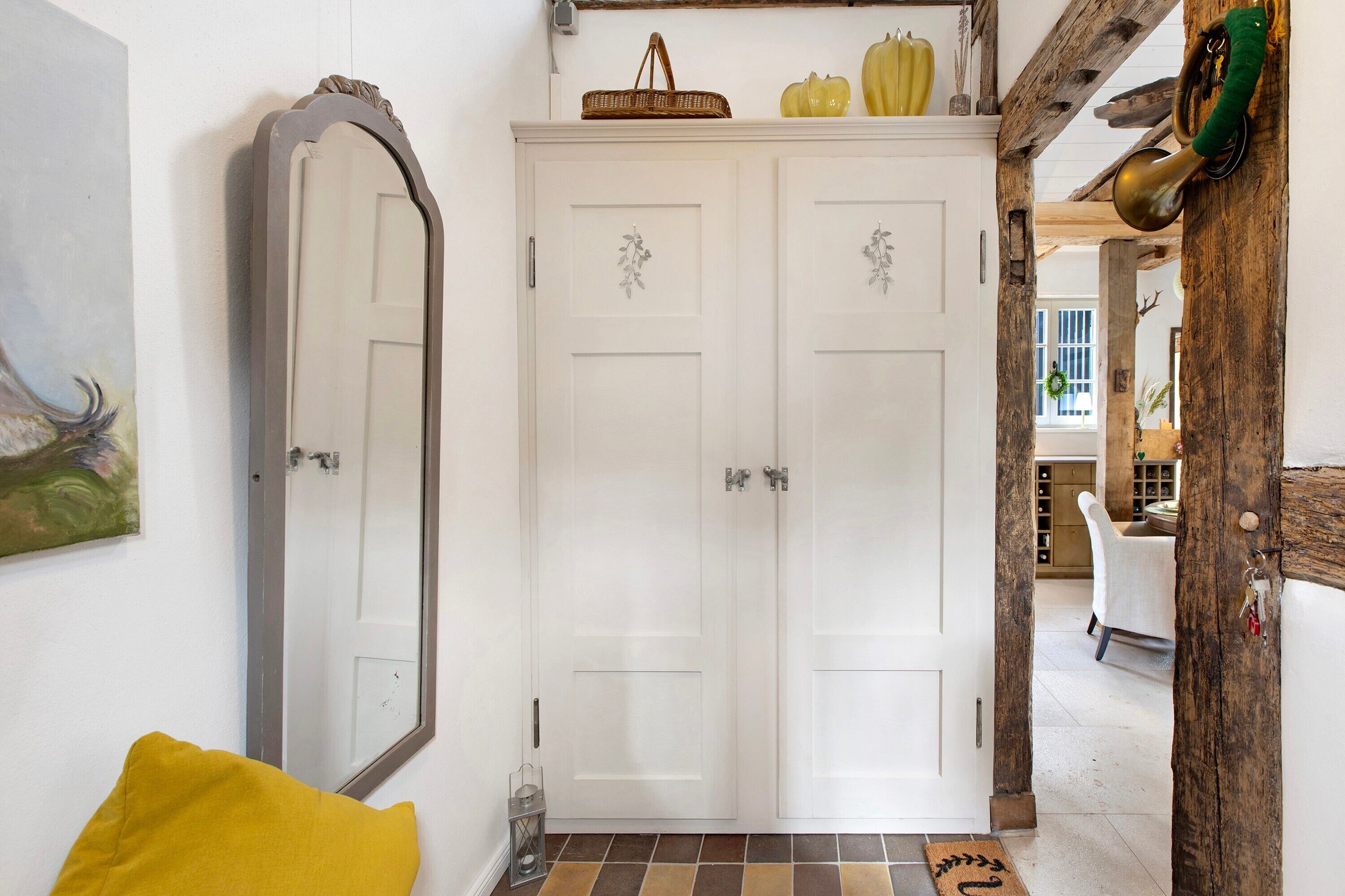 A hallway with a white door, a mirror, a yellow pillow, and a patterned rug.