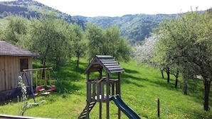 A playground with a slide and swings, surrounded by lush greenery and a wooden cabin. - Apartment 'Dischhansenhof' with Mountain View, Shared Garden and Wi-Fi (Glottertal)