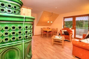 Een eetruimte met een houten tafel en stoelen, een bank, en een groot decoratief groen object.