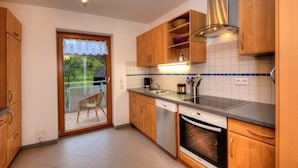 A kitchen with wooden cabinets, a dishwasher, an oven, a sink, and a window with a view of greenery. - Apartment 'Dischhansenhof' with Mountain View, Shared Garden and Wi-Fi (Glottertal)