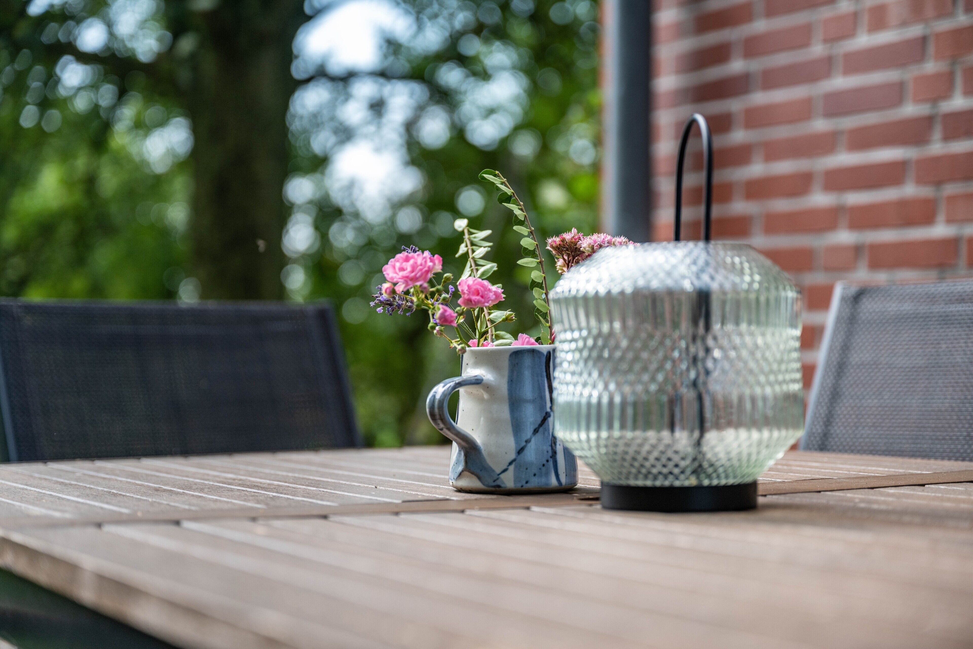A table with a decorative mug and a glass object, possibly a candle holder, with a plant in the mug.