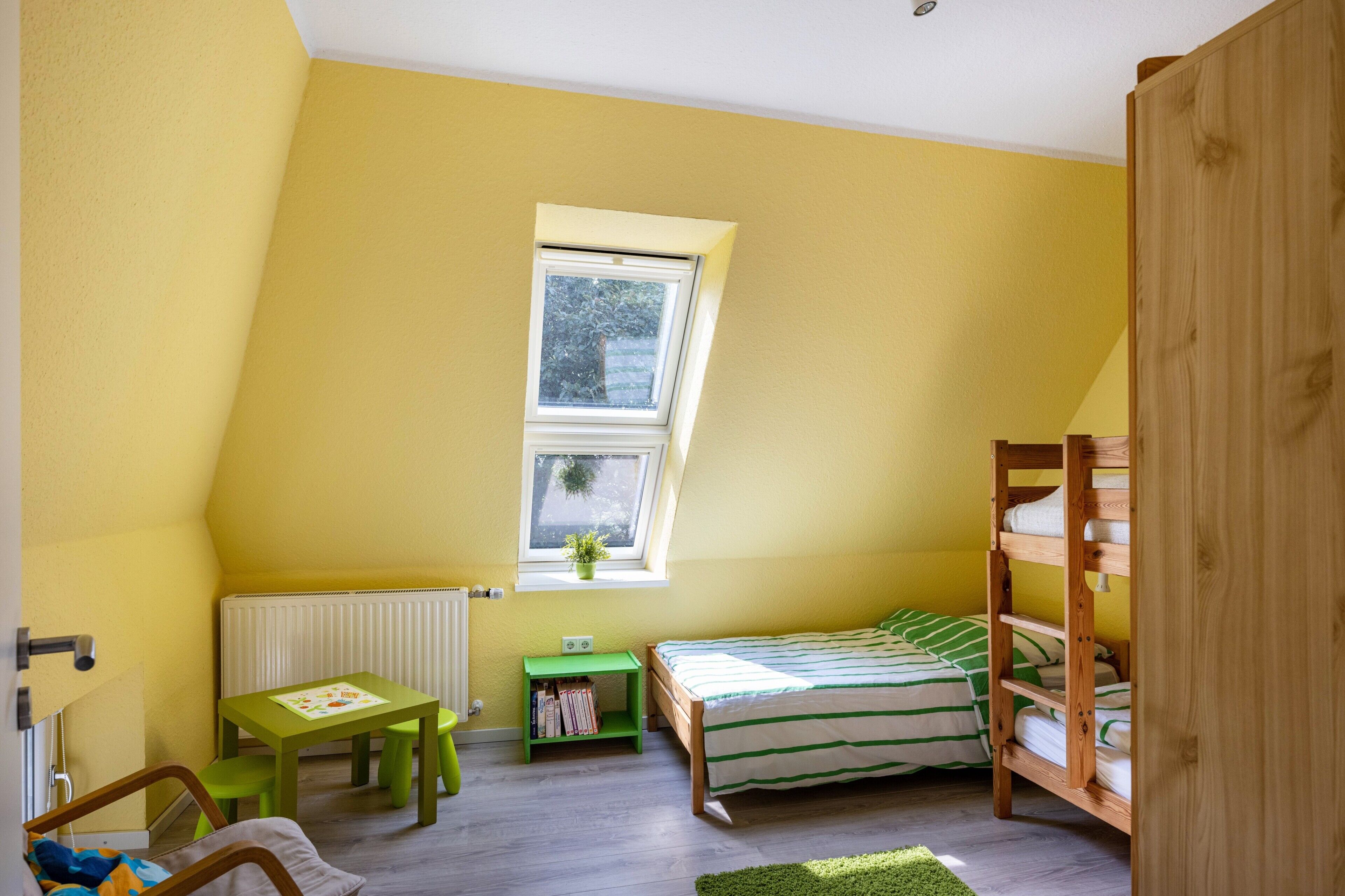 A room with a sloped ceiling, a window, a bunk bed, a desk with a chair, and a radiator.