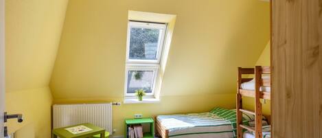 A room with a sloped ceiling, a window, a bunk bed, a desk with a chair, and a radiator.