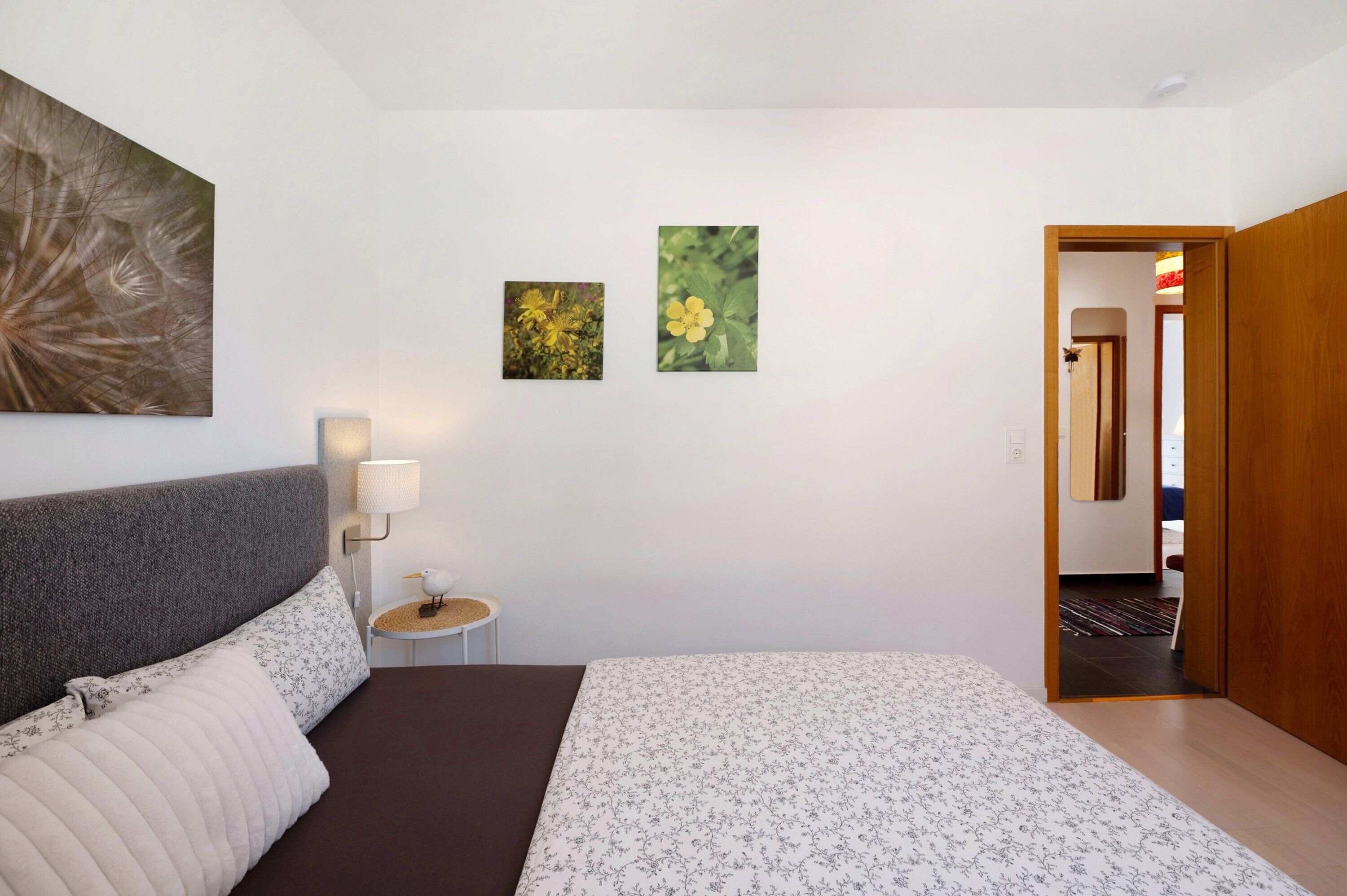A bedroom with a bed, a nightstand, a lamp, and two framed pictures on the wall.