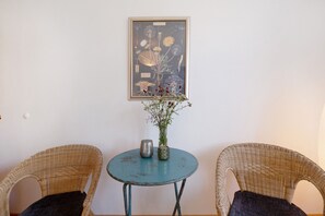 Une pièce comprenant deux fauteuils en osier, une petite table ronde, une illustration botanique encadrée et un vase rempli de fleurs.