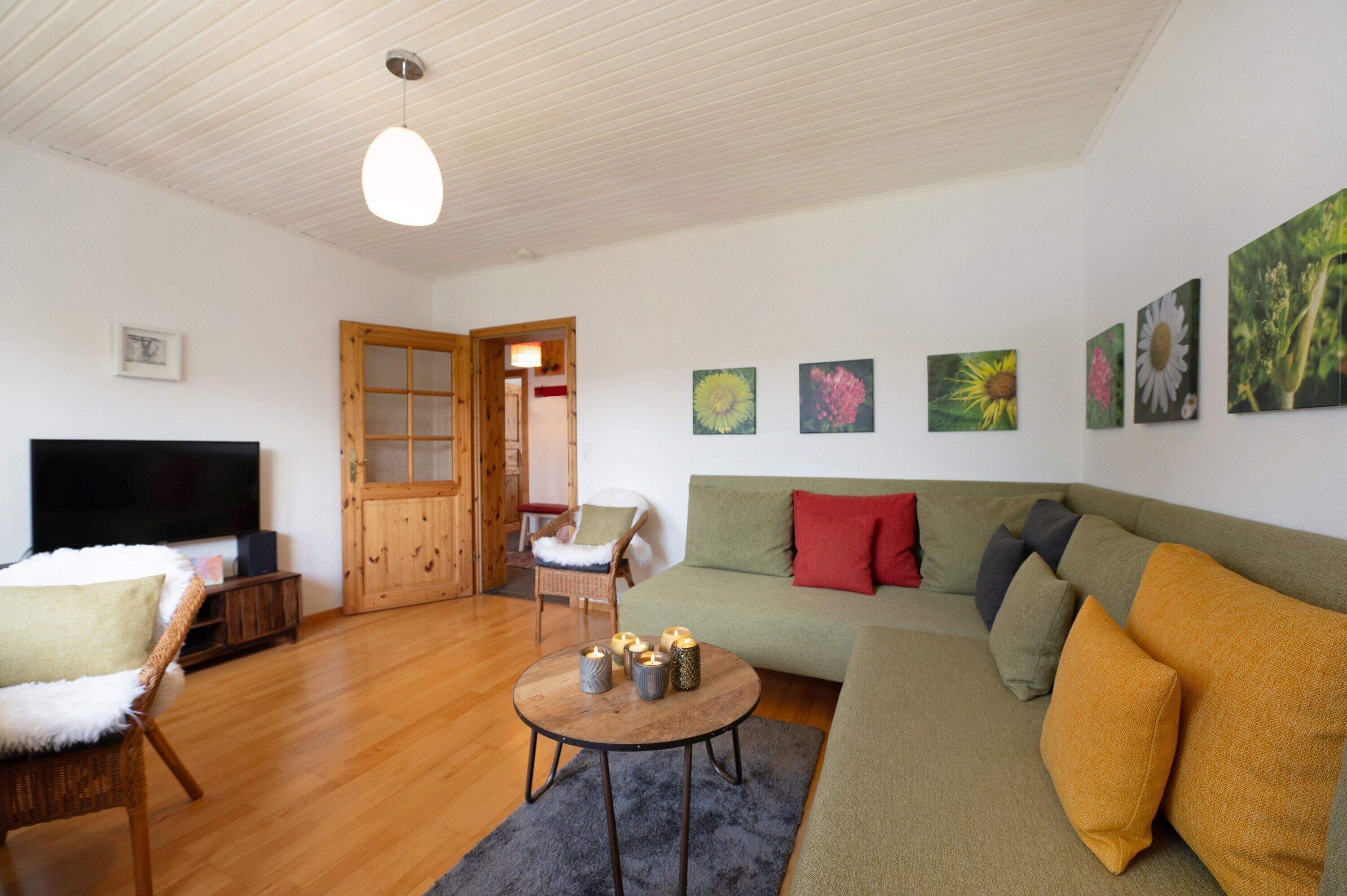 Een woonkamer met een televisie, een bank, een salontafel met kaarsen, een stoel en een deur naar een andere kamer.