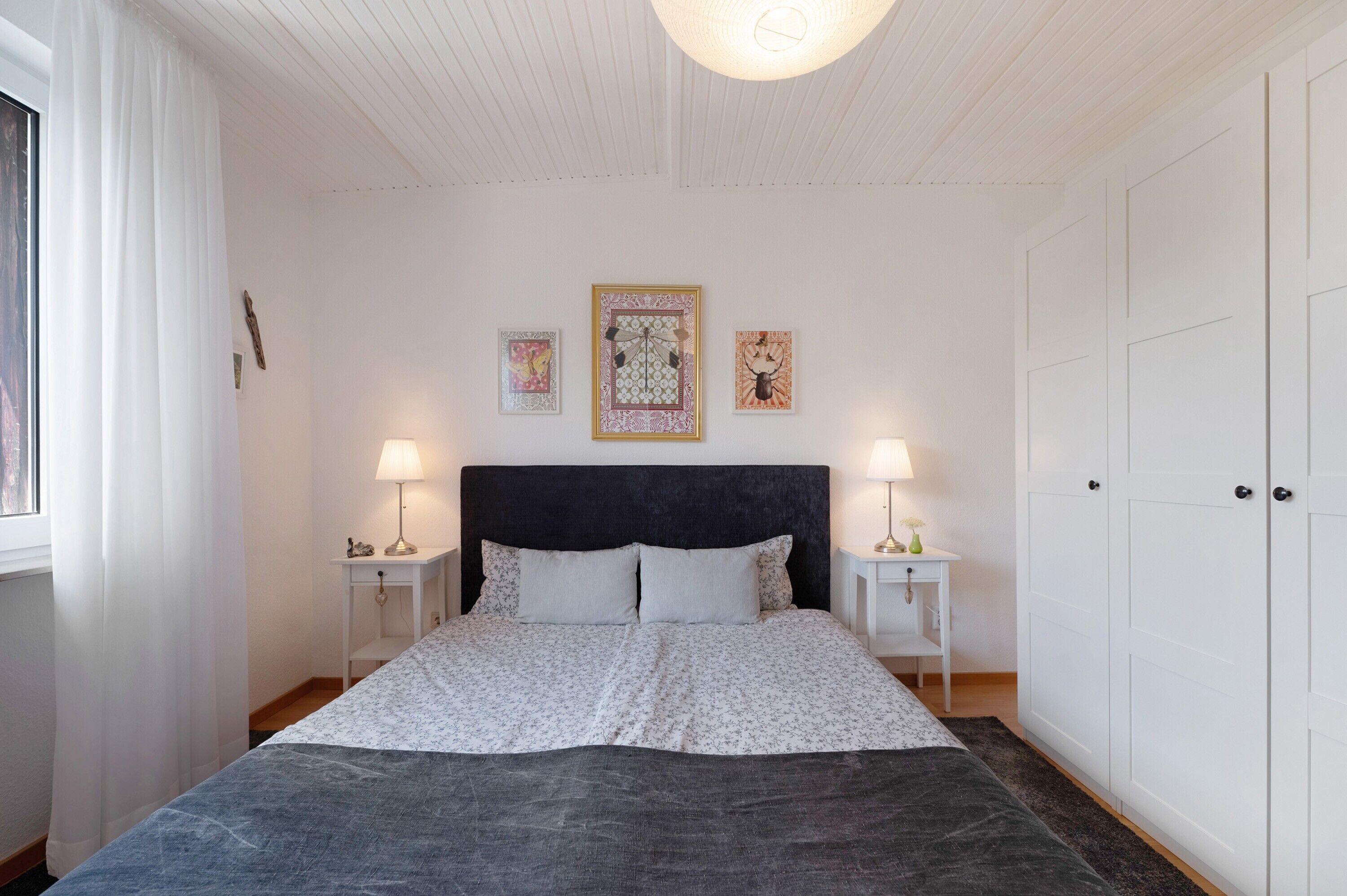 Una camera da letto con un letto, due comodini, un armadio e tre quadri appesi al muro.