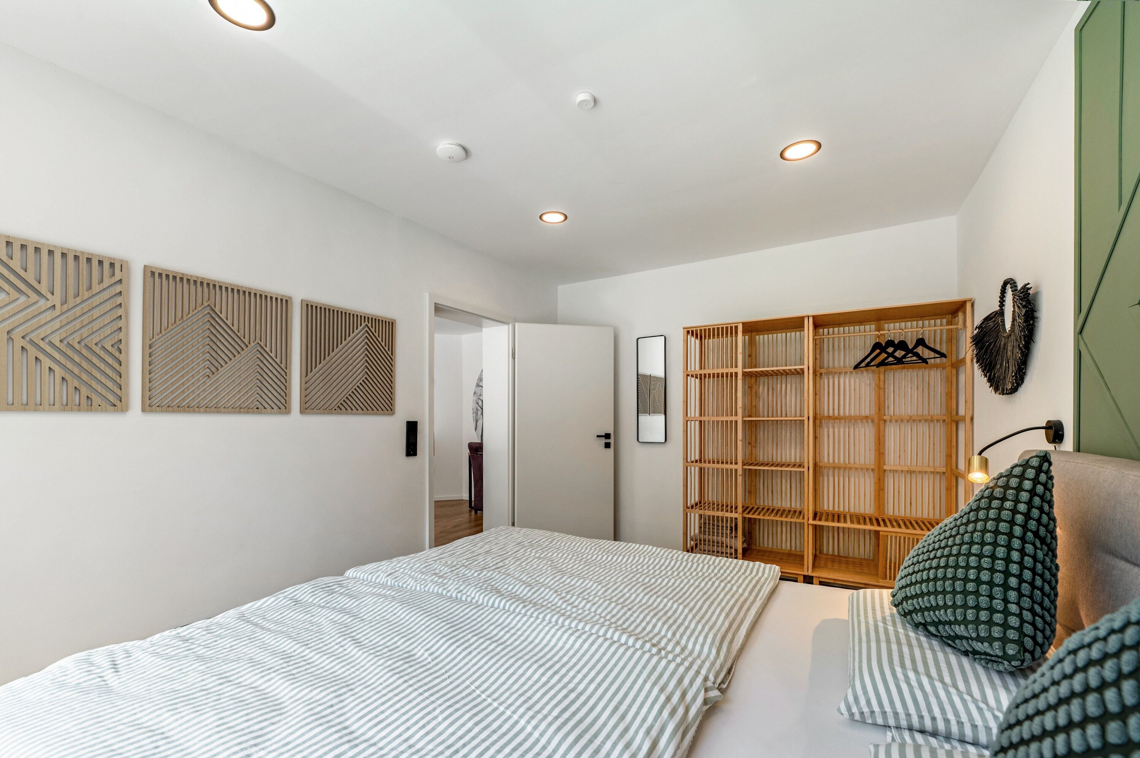 Ein Schlafzimmer mit Bett, Kleiderschrank, Spiegel und Kleiderhaken.