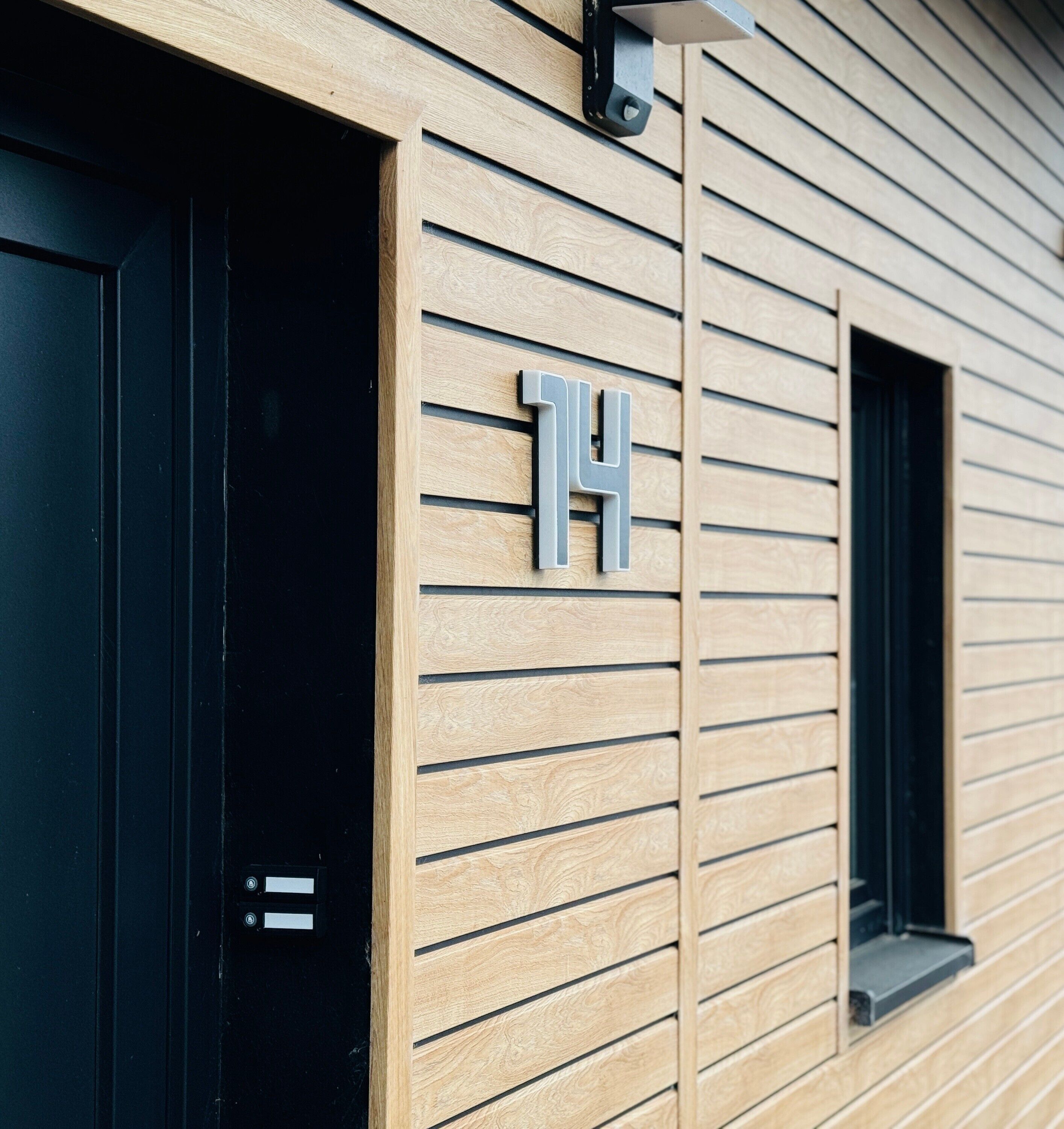 Une façade d’immeuble avec des panneaux de bois horizontaux, une porte noire et une fenêtre.