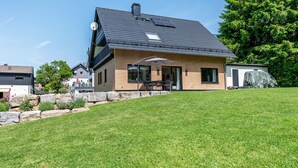 A modern house with a sloped roof, a covered patio, and a well-maintained lawn.