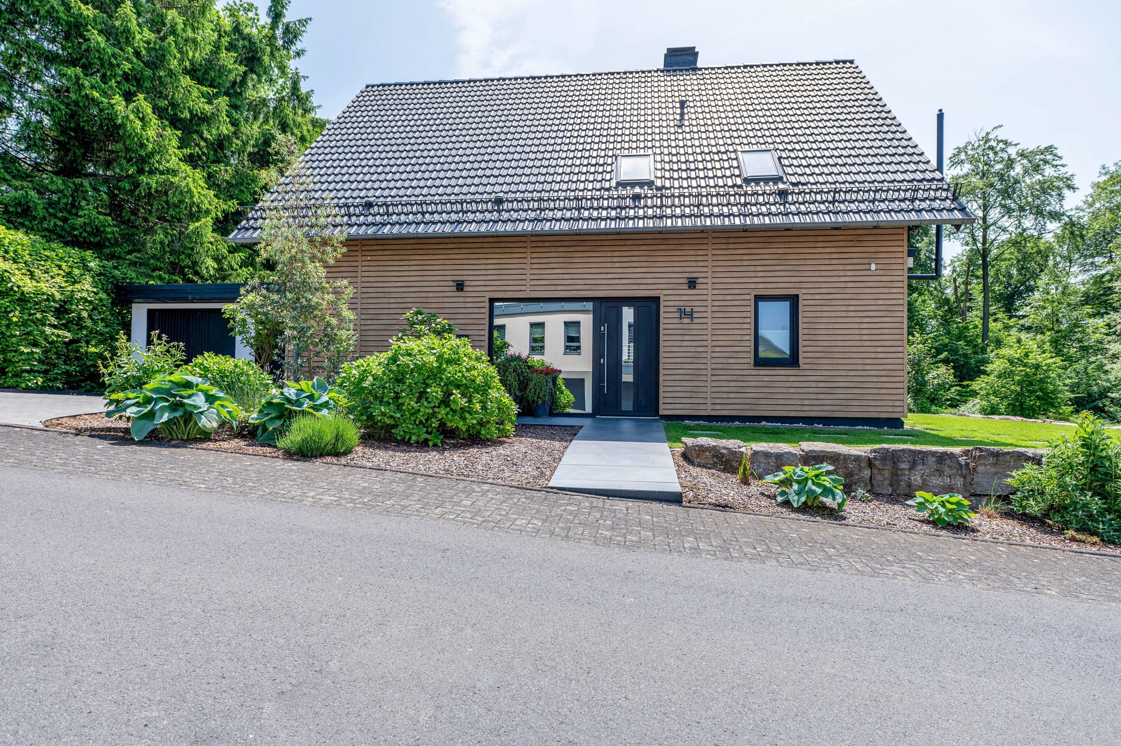 Ein modernes, zweistöckiges Haus mit Ziegeldach, Eingangsbereich und kleinem Garten.