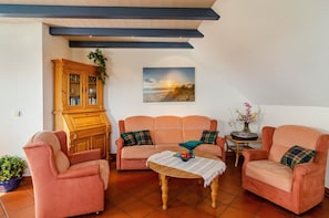 Una sala de estar con un sofá, sillones, una mesa de centro, un aparador y un cuadro en la pared.