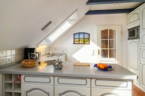 Una cocina con tragaluz, ventana con vistas, microondas y frutero sobre la encimera.